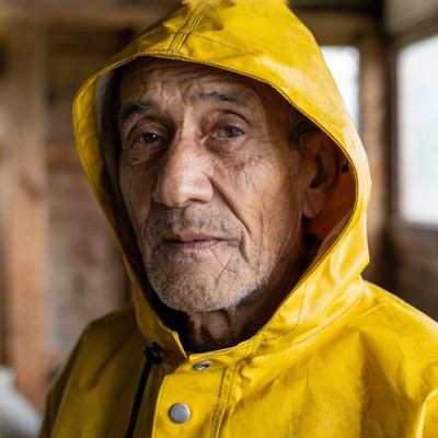 Close-up portrait of an elderly fisherman with a weathered face and grey stubble, wearing a yellow raincoat, soft overcast light from a window, shallow depth of field, 85mm photograph, generated by Ideogram V4