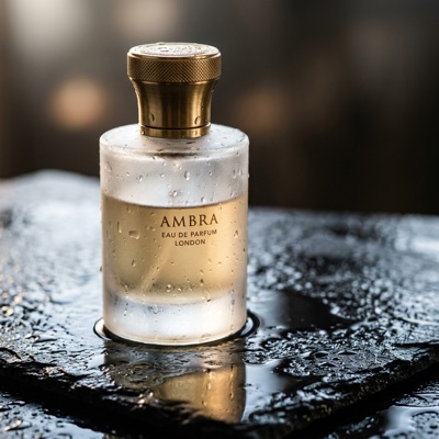 A frosted glass perfume bottle with a brass cap on wet black slate, droplets on the glass, soft rim light, reflections on the stone, studio product photography, generated by Nano Banana 2