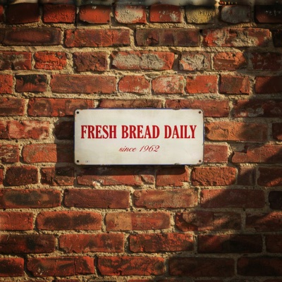 A vintage enamel sign on a brick wall that reads "FRESH BREAD DAILY" in bold red serif letters, with "since 1962" in smaller script below, morning sunlight, generated by Ideogram V4